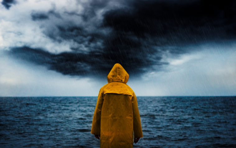 A person wearing a yellow rain jacket looks out at the ocean during a rainstorm.