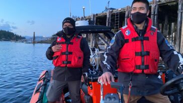 Two Coastal Nations Coast Guard Auxiliary members with life jackets on a boat.